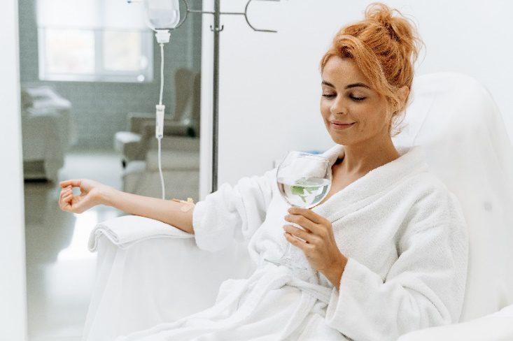 A woman in white robe holding wine glass.